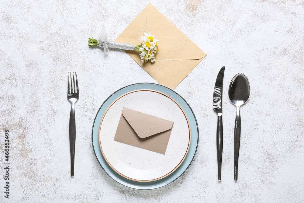 Beautiful table setting with wedding invitation and chamomile flowers on light background