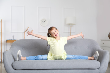 Wall Mural - Little girl doing leg-split on sofa at home