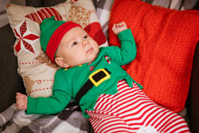 Christmas Concept Little Boy Cheerful Elf Looking Up Lies On Multi-colored Pillows In Gnome Costume. Santa's Little Helper