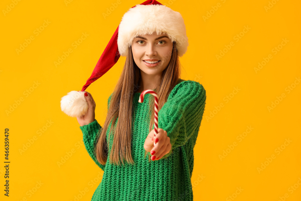 Beautiful young woman in Santa hat with candy cane on yellow background