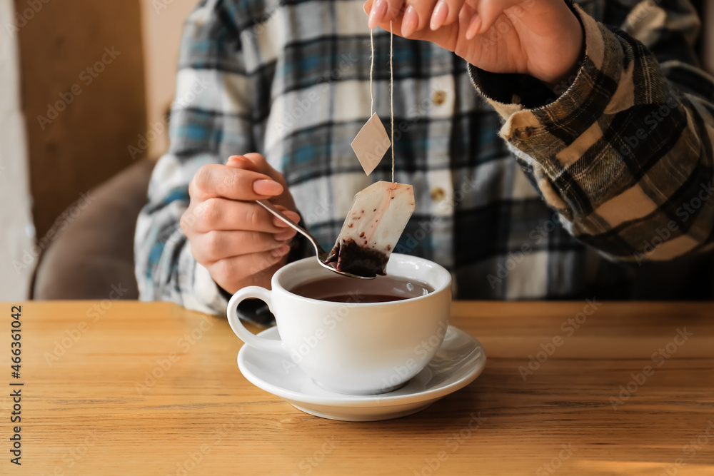 Woman brewing tea with bag in cup at table in cafe, closeup
