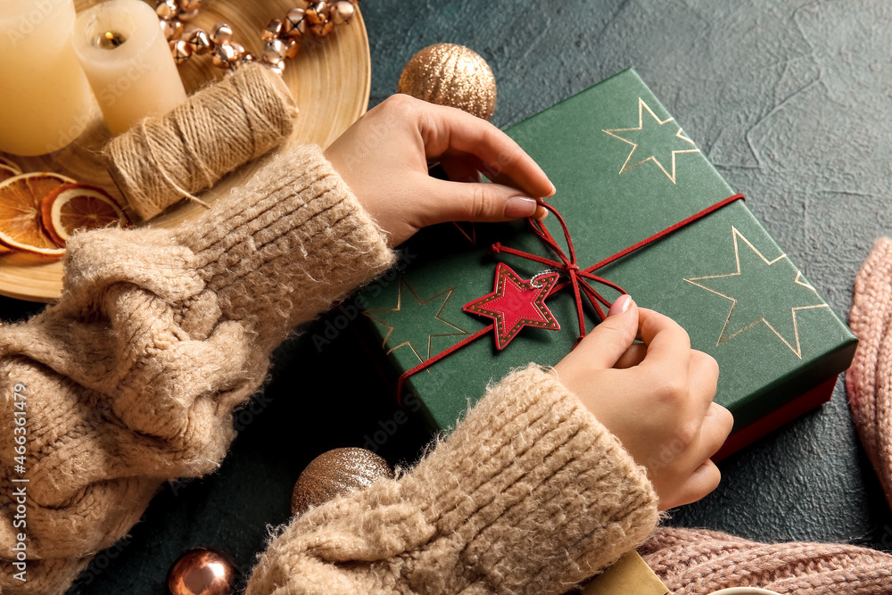 Woman decorating Christmas gift box on black background