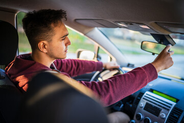 Wall Mural - Back view of young caucasian man adjusting the rear mirror in car while driving or parking real people travel concept