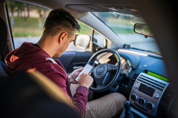 Wall Mural - Back view of young caucasian man checking mobile phone for messages or navigation app for destination while sitting in car driving or parking real people travel concept