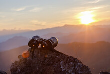 Binocular On Top Of Rock Mountain At Sunset Background