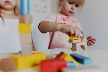 Two child girl sisters playing with colorful wooden toy building blocks