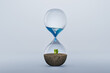 Hourglass with fresh water drop to green plant planting on dry land isolated background, metaphoric of saving water, Drought and Climate change.