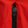 Black plastic zipper with metal slider in red nylon jacket close up