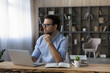 © fizkes - Thoughtful young successful businessman in eyewear looking in distance, considering problem solution, planning workday, creating new online project, working on computer in modern home office.