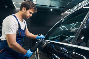 Repairman with orbital polisher fixing scratches on car side