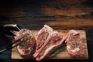 Wall Mural - three lovely raw marbled black Angus beef steaks flavored with a mixture of ground pepper and ready to cook and serve on a dark wooden background.