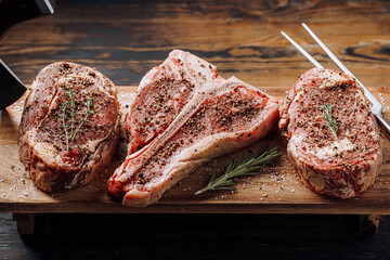 Wall Mural - three lovely raw marbled black Angus beef steaks flavored with a mixture of ground pepper and ready to cook and serve on a dark wooden background.