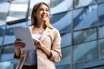 Wall Mural - Successful businesswoman using a digital tablet while standing in front of business building.