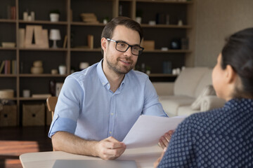 Canvas Print - Interested smiling professional male human resources manager employer in eyewear holding paper CV in hands, holding job interview with skilled female Indian candidate at meeting, recruitment concept.