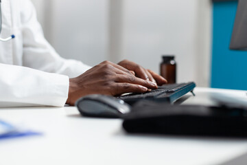 Closeup of african american doctor typing patient healthcare treatment on computer after analyzing sickness symptoms. Therapist man working at medical documents in hospital office