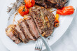juicy well-fried ribeye steaks on a white platter on a white marble surface with raspmarine and fried cherry tomatoes and peppers. steaks are sliced and ready to serve