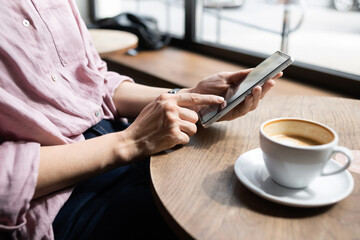 Wall Mural - Young woman using smartphone at cafe. Student girl texting on mobile phone at coffee shop. Communication, home work or study, connection, mobile apps, technology, lifestyle concept