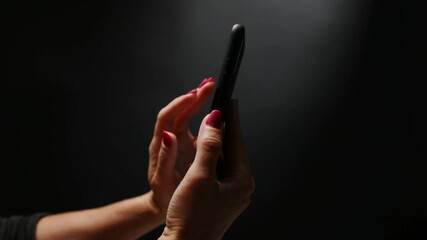 Female hand holding smartphone and scrolling screen down on black background. Online communication with cell phone using modern technologies