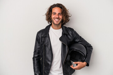 Young biker caucasian man holding a motorbike helmet isolated on gray background happy, smiling and cheerful.