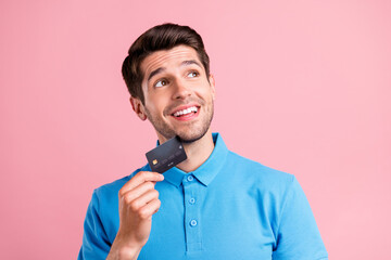 Photo of cute brunet millennial guy hold card look empty space wear blue t-shirt isolated on pink color background