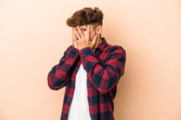 Wall Mural - Young arab man isolated on beige background blink through fingers frightened and nervous.