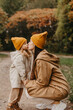 © Ananass - Young happy and smiling mom with her little daughter in arms hugging and kissing spending a weekend on a walk in autumn park. selective focus, noise effect, Autumnal mood