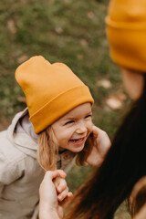 Young happy and smiling mom with her little daughter in arms hugging and kissing spending a weekend on a walk in autumn park. selective focus, noise effect, Autumnal mood