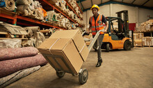 African Female Warehouse Worker Moving Boxes With A Dolly