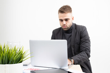 A guy in business clothes is working on a laptop at a table on a white background