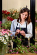 Young woman florist working in flower shop, carefully arrangingfresh spring flowers for bouquet. attractive confident and professional florist in apron is cutting flower petals with scissors.