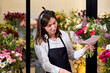 Good-looking Florist in apron works with colors. Flower seller chooses flowers for future bouquet. Flowers shop worker in flower shop, decorating and arranging different unusual blooming flowers