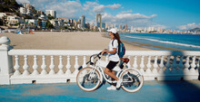 Happy Woman Tourist With Electric Bicycle Over Background Levante Beach Overlooking Panorama Of Benidorm City. Traveler Concept