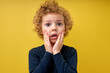 Portrait of surprised kid boy in shock, touching cheeks, stand with widely opened mouth and eyes, caucasian child looking at side, saw something, isolated on yellow studio background. copy space