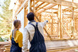 View From Back On Constructors In Working Clothes Explore Construction Documentation on Building Site Near The Wooden Building Constructions. Building and designing wooden frame house concept