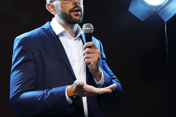Motivational speaker with microphone performing on stage, closeup. Space for text