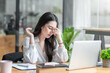© amnaj - Young Asian woman feeling migraine head strain. Tired, Overworked businesswoman financier while working on laptop computer in office.