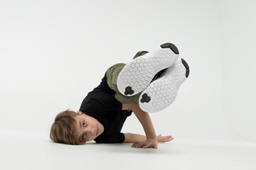 Isolated young cute Russian teenage boy in black t-shirt hip hop break dancer dancing in studio in white background, performing stunt baby freeze of downrock breakdance looking into the camera