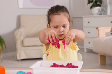 Poster - Cute little girl playing with bright kinetic sand at table in room