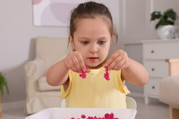 Poster - Cute little girl playing with bright kinetic sand at table in room