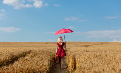 Canvas Print - Blonde girl in red dress with umbrella and suitcase on wheat field