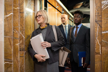 Poster - Group of contemporary intercultural co-workers with documents waiting for elevator while standing in corridor of office center