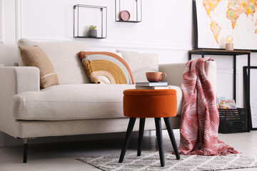 Wall Mural - Stylish ottoman with books and cup of coffee near sofa in light living room