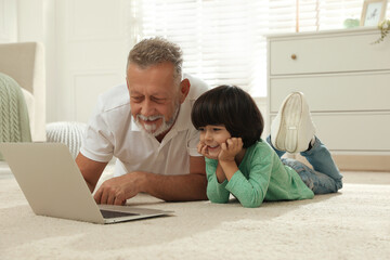 Poster - Happy grandfather and his grandson using laptop together on floor at home