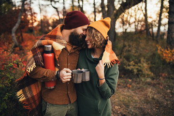 Happy couple in love drinking tea from thermos in beautiful autumn forest.