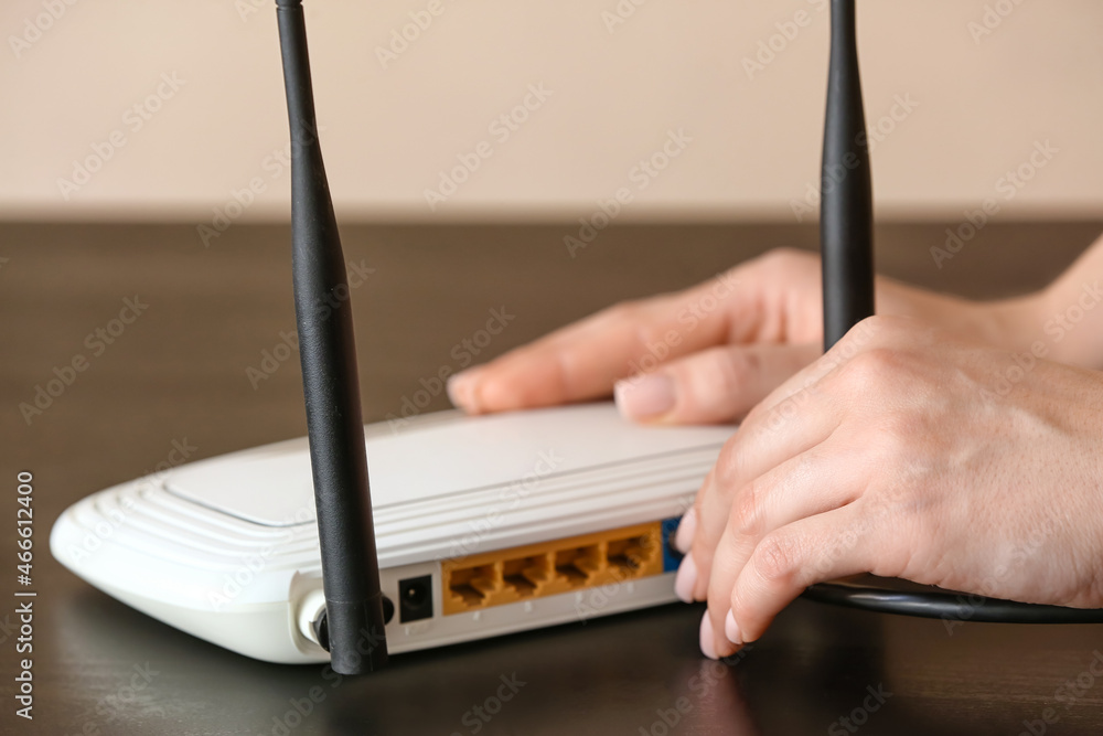 Woman inserting ethernet wire into wi-fi router on table in room