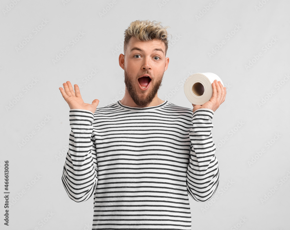 Surprised young man with toilet paper on light background