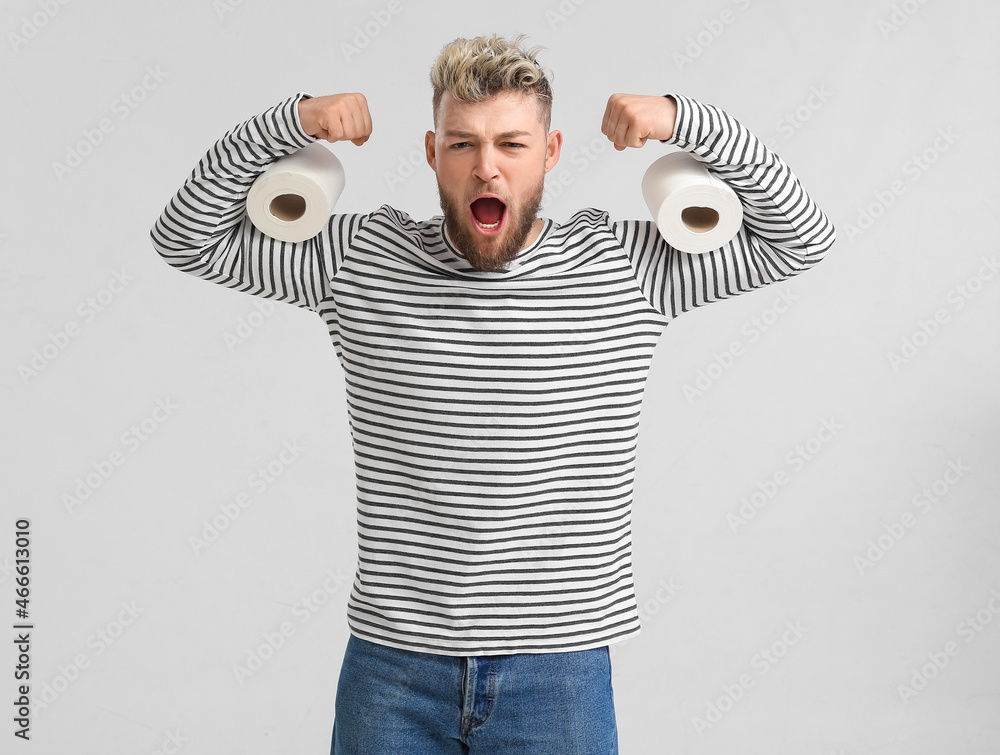 Emotional muscled man with toilet paper on light background