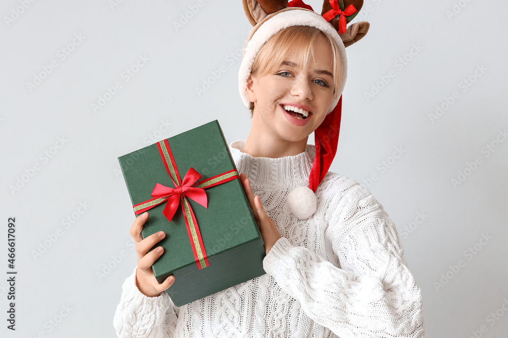 Beautiful young woman with Christmas gift on light background