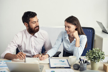 Canvas Print - Positive creative young colleagues sitting at table with papers and brainstorming about business project in office