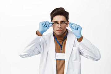 Wall Mural - Doctor in medical robe and glasses, trying to read with glasses, looking confused, reading, standing over white background